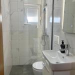 Badezimmer mit Dusche, Waschbecken und Toilette. Weiße Fliesen und Spiegel.