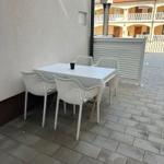 Terrasse mit weißem Tisch und vier Stühlen. Hintergrund: Gebäude mit Balkon.