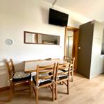 Essbereich mit Holztisch, vier Stühlen und Wandfernseher.