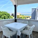Terrasse mit weißem Tisch und Stühlen, Blick auf See und Berge.