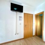 Wohnraum mit Wandfernseher, Holztür und angrenzender Tür.