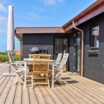 Terrasse mit Holztisch, Stühlen und Sonnenschutz neben einem Haus mit dunkler Fassade.