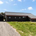 Schwarzes Haus mit Garage und grünem Grundstück unter blauem Himmel.