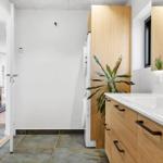 Badezimmer mit Waschbecken, Spiegelschrank und Pflanze. Tür führt in Wohnbereich.