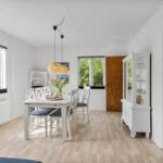 Dining room with white table, chairs, and wooden floor. Windows, cabinet, and plant visible.