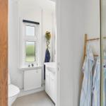 Bathroom with shower, sink and toilet. Window with plants and towel rack.