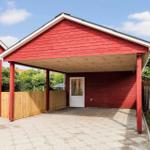 Red carport with wooden cladding and white door. Paved ground and wooden fence.
