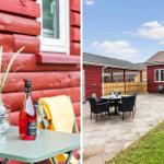 Red wooden house with patio and garden. Table with wine and grass stems.