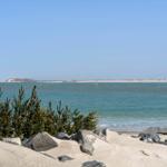 Beach with sand dunes and rocks, view of the sea and an island in the background.