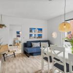Living and dining area with blue sofa, white table and chairs, wall pictures and hanging plants.