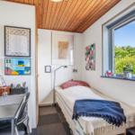Schlafzimmer mit Bett, Schreibtisch und Fensterblick auf Grün.