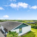 Modernes Haus mit grünem Garten und Blick auf Felder unter blauem Himmel.