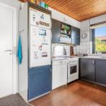 Küche mit Kühlschrank, Spüle und Fenster. Holzdecke und Boden.