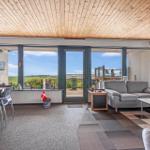 Wohnzimmer mit großem Fensterblick auf Landschaft und Terrasse mit Möbeln.