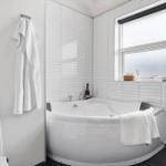 Bad mit Eckbadewanne, Fenster und weißen Fliesen.