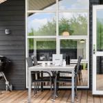 Terrasse mit Grill, Tisch und Stühlen. Große Fenster und Tür führen ins Haus.