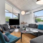 Wohnzimmer mit Sofa, Sessel und Kamin. Große Fenster und Holzboden.
