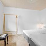 Schlafzimmer mit Bett, Kleiderständer und Stuhl an Fenster