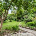 Garten mit gepflasterter Weg, Bäumen und Blumenbeeten.