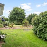 Grüner Garten mit Bank, Sträuchern und Baum. Hausansicht mit Dach und Wand.