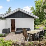 Haus mit Terrasse, Gartenmöbel und blühenden Sträuchern.