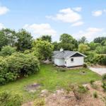 Wohnhaus mit Garten und Wald im Hintergrund unter blauem Himmel.
