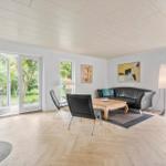 Wohnzimmer mit Sofa, Tisch und Stühlen. Holzfußboden und Fenster zur Außenterrasse.