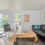 Wohnzimmer mit Sofa, zwei Stühlen, Tisch und Fenstern zum Garten.