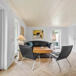 Wohnzimmer mit schwarzer Couch, zwei Stühlen und Holzboden. Große Fenster und Wandbild.