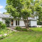Ein Haus mit Garten, Bäumen und einer Bank im Freien.