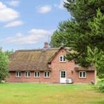 Rotes Backsteingebäude mit strohgedecktem Dach und weißen Fenstern in grüner Umgebung.