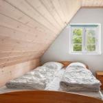 Schlafzimmer mit Dachschrägen, Holzwänden und Fenster mit Blick auf Bäume.