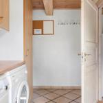 Waschmaschine in Küche mit Holzregalen und Türöffnung.