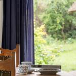 Holztisch mit Tassen und Tellern vor Fenster mit Blick auf Garten.