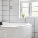 Eine Badewanne in einem Badezimmer mit Fliesenwand und Fenster.