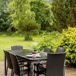 Helle Außenterrasse mit Tisch und Stühlen, umgeben von Grün und Bäumen.