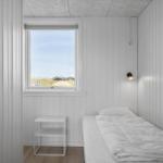 Ein Schlafzimmer mit weißem Bett, Fenster und Nachttisch.