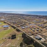 Luftbild von Ferienhäusern am Meer mit Golfplatz und Windkraftanlagen im Hintergrund.
