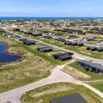 Aerial view of holiday homes near the sea with green fields and a pond.