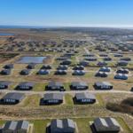 Aerial view of holiday homes near coastal area with ponds and open fields.