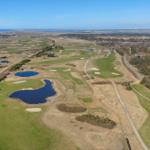 Luftbild eines Golfplatzes mit Seen und Sandbunkern, umgeben von Wiesen und Bäumen.