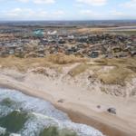 Aerielansicht von Strand, Dünen und Wohnsiedlung an der Küste.