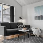 Wohnzimmer mit grauem Sofa, Tisch und Teppich. Große Fensterfront mit Blick auf Terrasse.