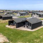 Modernes Ferienhaus mit Terrasse und Garten, umgeben von Gras und Dünen.