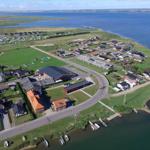 Aerial view of coastal village with houses, green fields, and water.