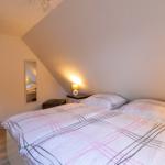 Schlafzimmer mit Doppelbett, Nachttisch und Spiegel an geneigter Wand.