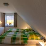 Schlafzimmer mit grün-weißem Bettbezug, Fenster mit Jalousie und Nachttische.