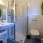 Badezimmer mit Dusche, Waschbecken und Toilette. Fliesenboden und Spiegelschrank.