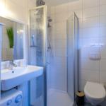 Badezimmer mit Dusche, Waschbecken und Toilette. Fliesenwand und Spiegel sichtbar.