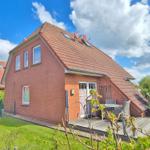 Rotes Backsteinhaus mit Terrasse und Garten unter blauem Himmel.